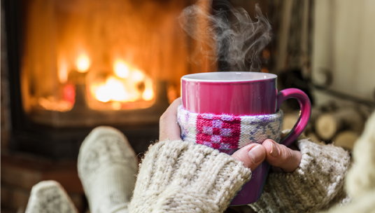 Persoon met mok in handen zit voor de openhaard.