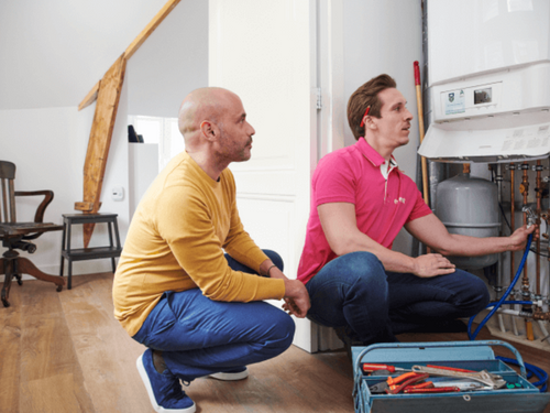 Twee mannen knielen bij een cv-ketel terwijl een monteur onderhoud uitvoert.