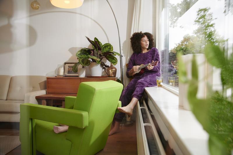 Vrouw zit bij een warme radiator en kijkt naar buiten.