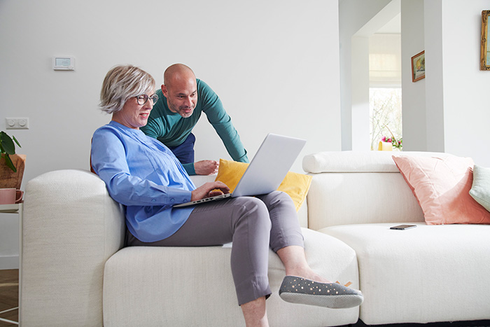 Vrouw zit op bank met een laptop op haar schoot, en een man kijkt mee