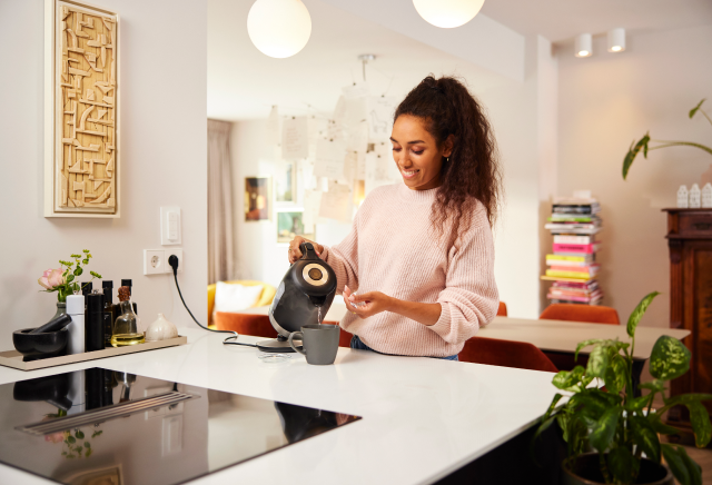 Vrouw schenkt water in kop in keuken