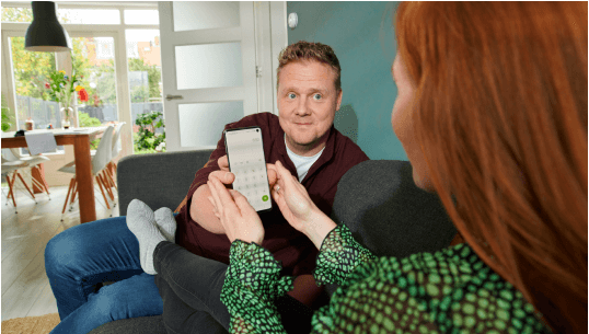Een man laat de telefoon zien aan een vrouw, ze zitten op de bank.