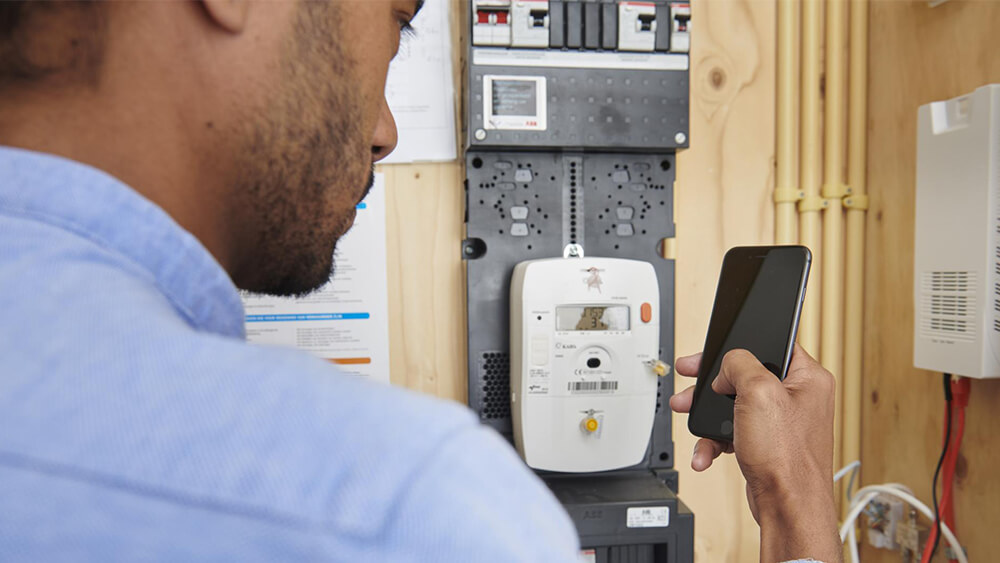Man staat met zijn telefoon bij de meterkast.