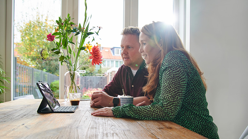 Man en vrouw zitten aan keukentafel en kijken naar subsidie voor isolatie op een iPad.