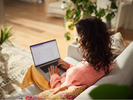 Een vrouw zit op de bank met laptop op schoot