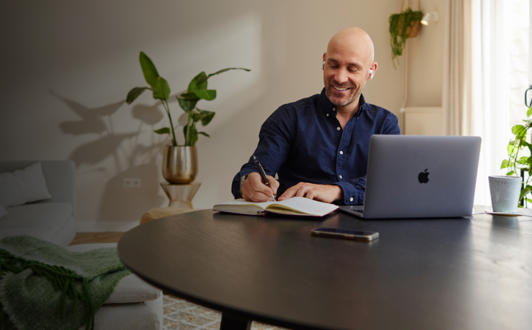 man aan ronde tafel achter laptop met notitie blok