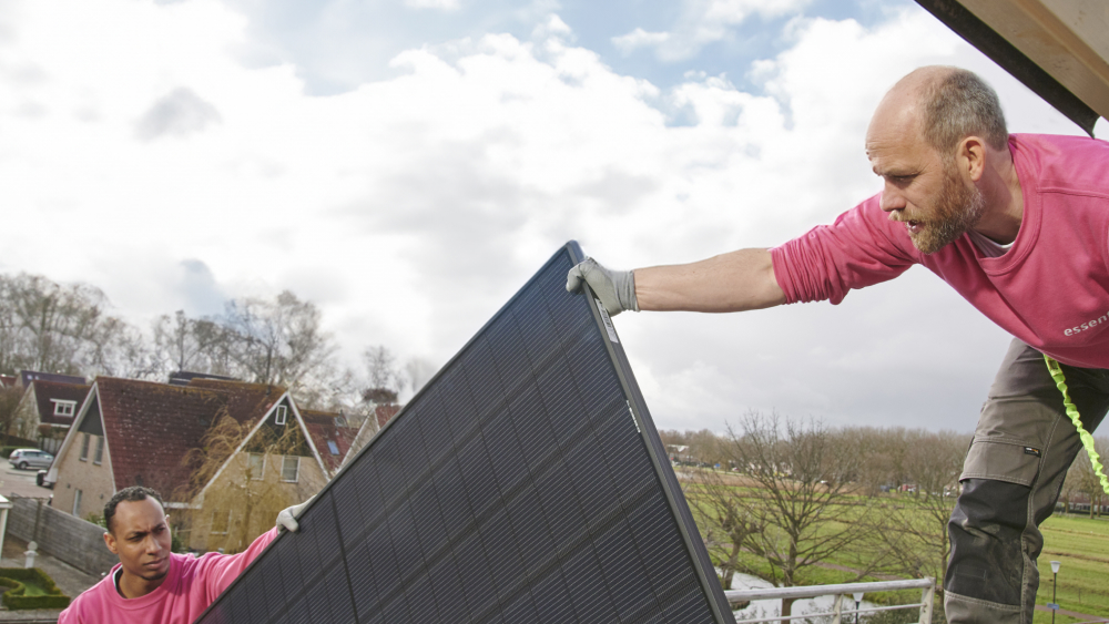 Twee monteurs dragen een zonnepaneel op het dak.