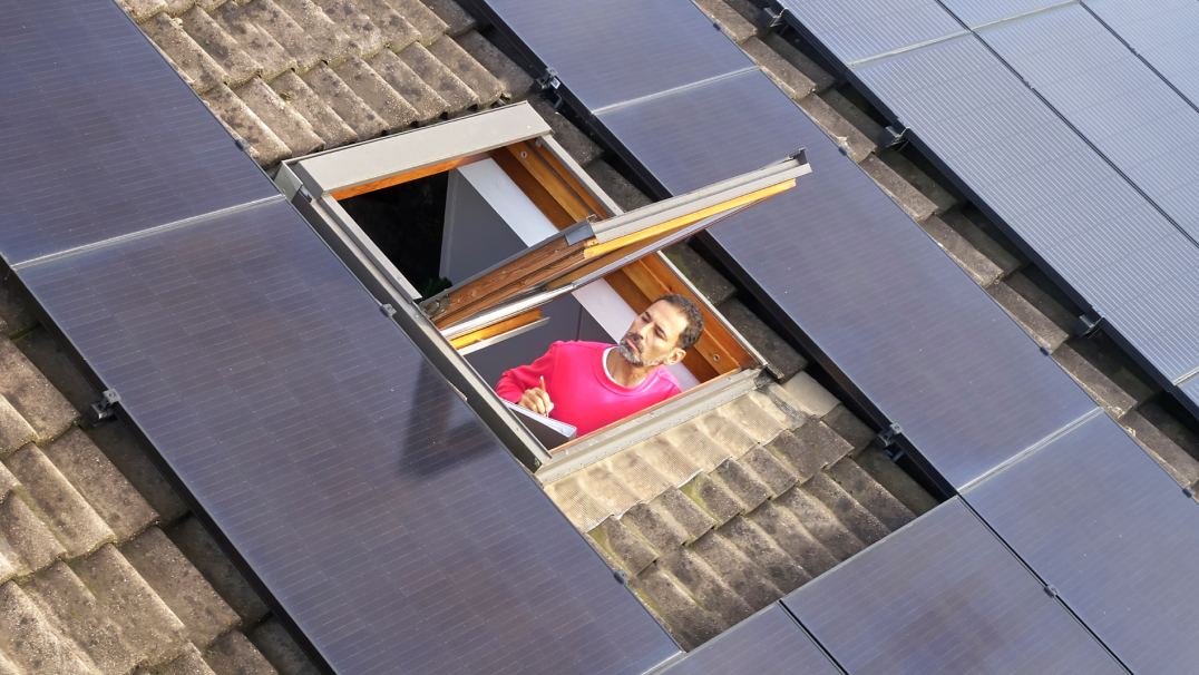 Een monteur van Essent kijkt vanuit een dakraam naar zonnepanelen