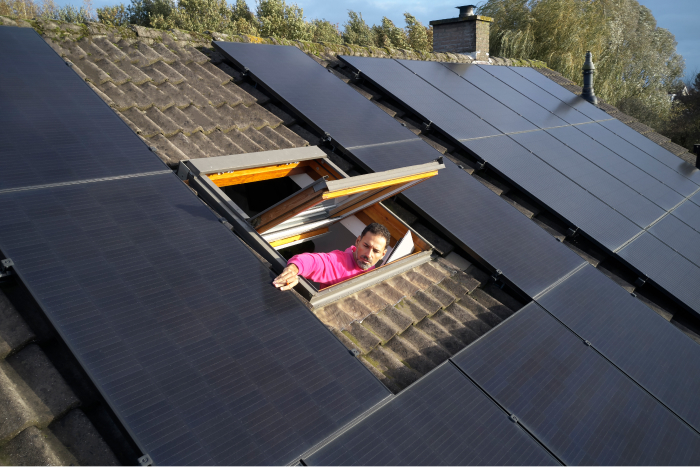 De monteur van Essent raakt een zonnepaneel aan vanuit een dakraam