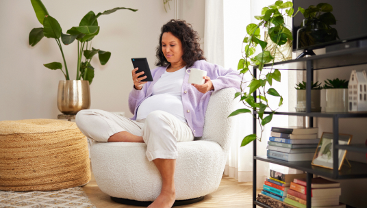 zwangere vrouw drinkt koffie en chect telefoon/tablet