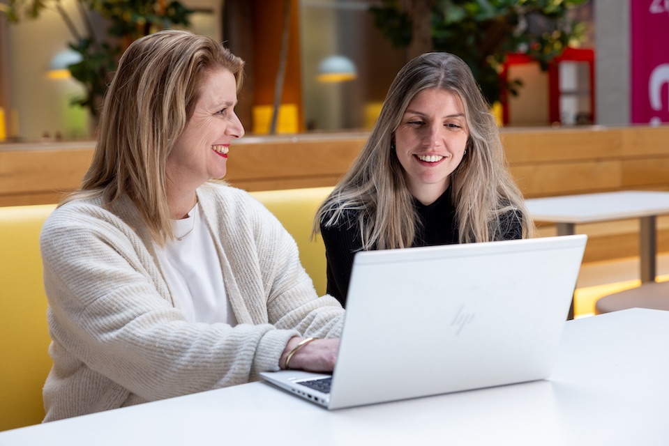 Twee vrouwelijke medewerkers van Essent glimlachend achter een laptop