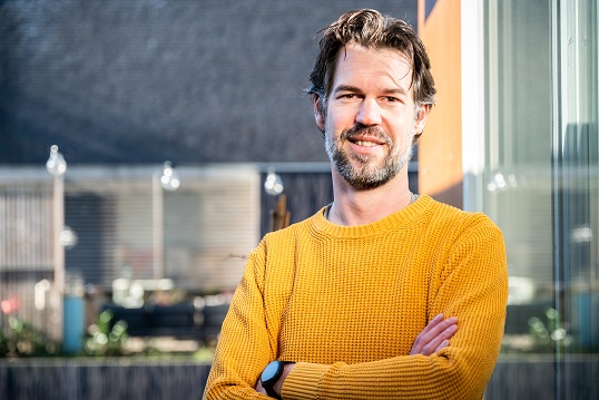 Man met gele trui kijkt lachend.