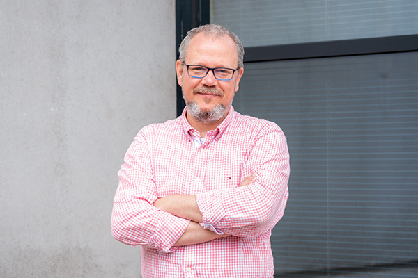 Man met roze bloes en bril kijkt.